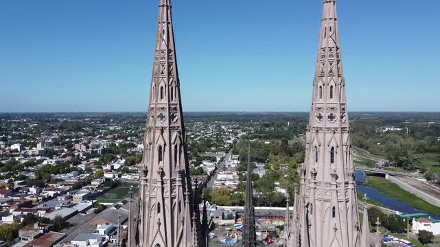 Cinematographic shot crossing the towers of the Basilica de Lujan revealing the course of the Lujan river and the city on a sunny day in Argentina.