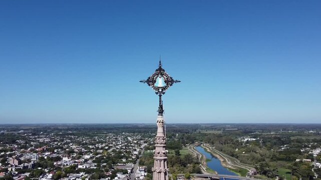 Circular aerial shot over the cross with the image of the virgin at the tip of the Basilica de Lujan, showing the city and the countryside in Buenos Aires.