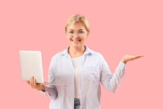 Happy young female programmer with laptop pointing at something on pink background