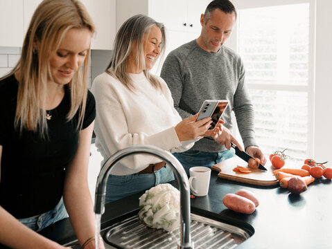 Teenage daughter helping dad prepare food by washing vegetables while mum on the phone