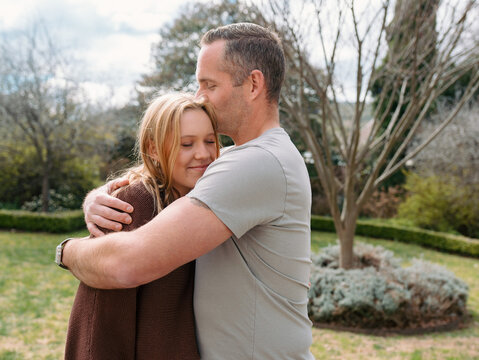 Father hugging teenage daughter in the garden and giving her a kiss in her hair