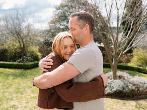 Father hugging teenage daughter in the garden and giving her a kiss in the forehead