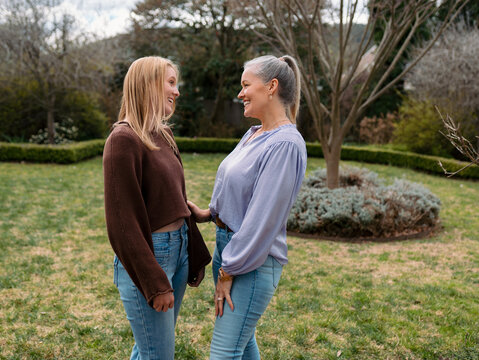 Mum and teenage daughter stands closely in the backyard looking at each other