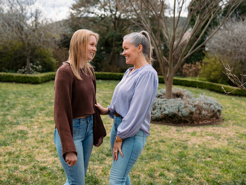 Mum and teenage daughter stands closely in the backyard looking at each other