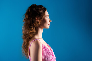 Young woman profile portrait in pink dress against a blue background, side view beauty portrait conveying calm confidence and elegance © deagreez