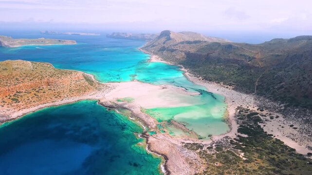 Breathtaking Balos Lagoon Crete. Aerial 4K. Drone reveal from Gramvousa island to turquoise shallow water with yacht and deep blue sea. Orange rocks contrast. Wild Gramvousa scenery. Greece summer 