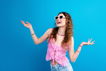 Young woman in pink top and sunglasses smiling joyfully against bright blue background — summer...