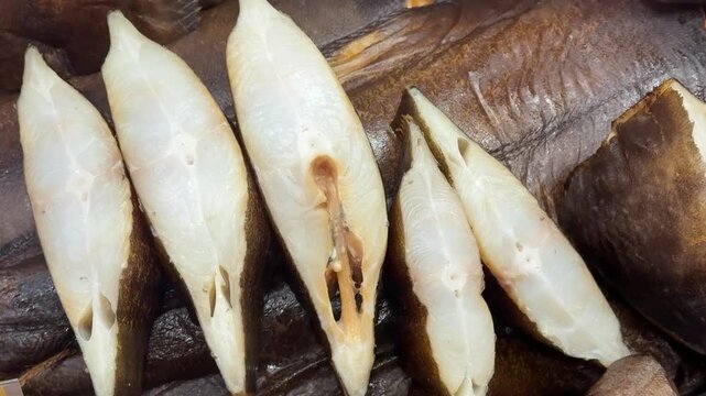 Cold smoked halibut steaks on counter, close-up of glistening white flesh and brown skin on chilled tray, market display suggests