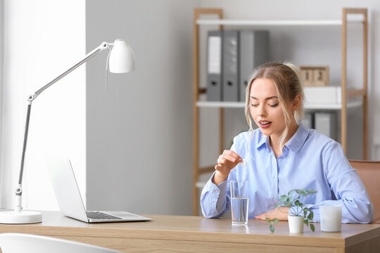 Young businesswoman putting soluble tablet into glass of water in office