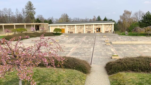 Wide view of Lidice memorial courtyard with blooming trees and clean stone layout under soft sky. Historic location in the Czech Republic expressing remembrance, calm and quiet atmosphere.