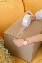 Obraz premium Woman taping cardboard box in office on moving day, closeup