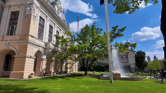 Wide view of Iasi City Hall courtyard with green tree, fountain and flagpoles on a bright sunny day in Stefan cel Mare area