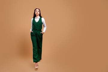 Confident businesswoman in green pinstripe suit walking with hands in pockets against warm brown...