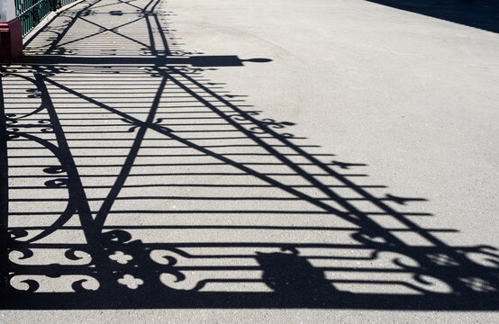 Ornate sharp patterned shadows of a gate and fence on a grey background