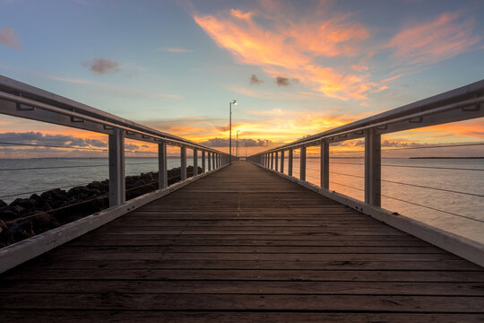Wooden jetty stretching over water with cloudy sunrise sky