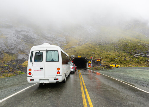 Vehicles queued to enter a road tunnel through a mountain with low clouds
