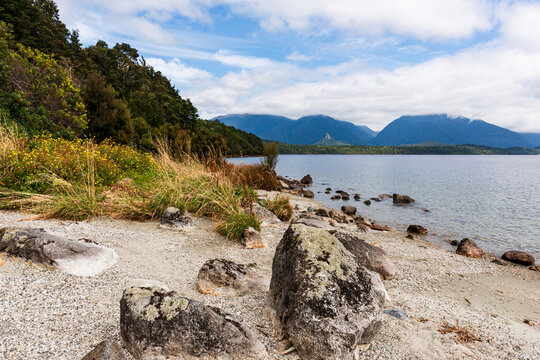 Lakeside sandy and stony beach with rocks and distant mountains