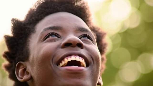 Extreme close-up video of a young person with luminous dark skin & coiled hair, laughing joyfully against a creamy bokeh background, bathed in golden hour light. Profound happiness concept