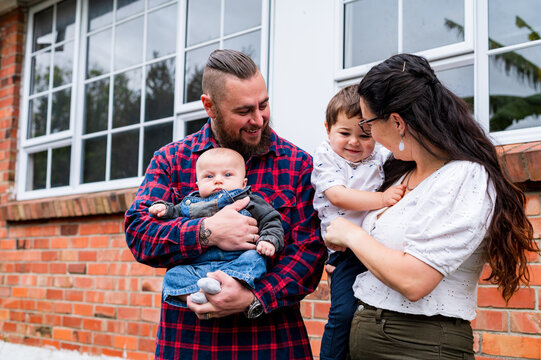 Happy couple standing in front of the brick walls holding an infant and toddler son