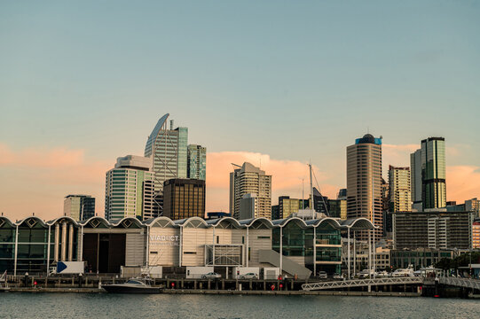 City skyline displays tall buildings by the water with boats in the dock as the sun sets