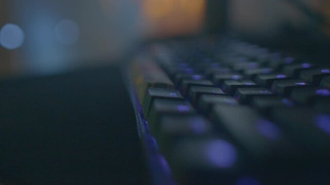 Purple glow on desk setup, Backlit computer keyboard illuminated by purple LED with artistic focus, Detailed view of glowing keyboard on desk featuring purple lighting and artistic background effects 