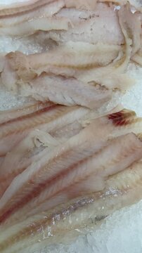 Thawed cod fillet on ice stacked on shallow crushed ice at supermarket counter, pale flesh glistening with visible moisture