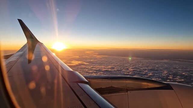 Breathtaking cinematic perspective from passenger aircraft window featuring metallic wing soaring above fluffy white clouds during vibrant golden sunrise at high altitude.