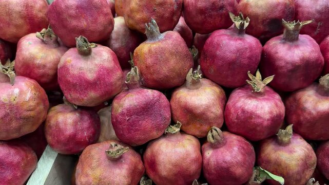 Ripe pomegranate fruits piled together, vibrant close-up of red skins and dried crowns, market stall arrangement with rustic