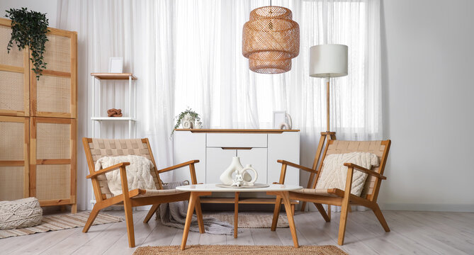 Interior of light living room with wooden armchairs, table and commode
