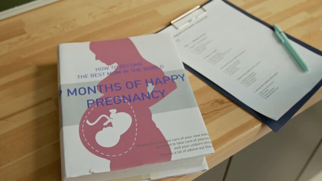 No people arc close-up of pregnancy guide book with silhouette of expecting mother and baby fetus in womb, and multiple choice test paper in reproductive health education classroom at high school