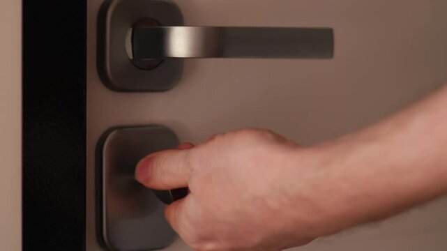 Close-up of a hand turning a thumb turn lock and pressing the door handle. Detailed shot of a person unlocking and opening a modern entrance door from the inside.