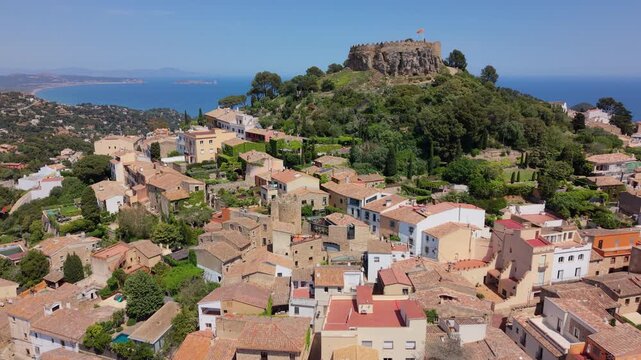 rone shot moving towards the medieval fortress of Begur, showing the coastal landscape of Costa Brava and the historical ruins under a clear blue sky.