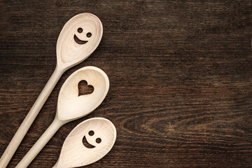 Wooden spoons with smiley faces and heart shapes on a dark wooden table during daylight hours