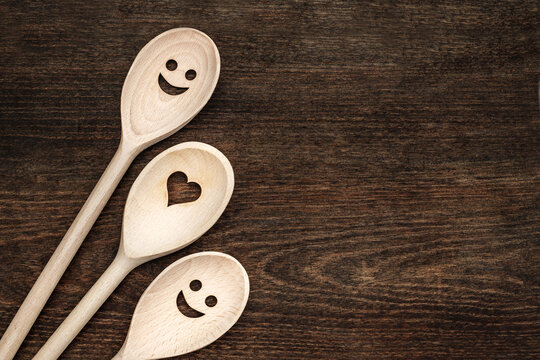 Wooden spoons with smiley faces and heart shapes on a dark wooden table during daylight hours