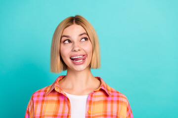 Fototapeta premium Playful young woman making a silly face and looking up against a turquoise background in a colorful plaid shirt portrait