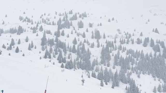 Ski lift rising above snowy slopes in Courchevel, France, surrounded by foggy alpine scenery during winter snowfall, with crowds of skiers descending the busy ski sl