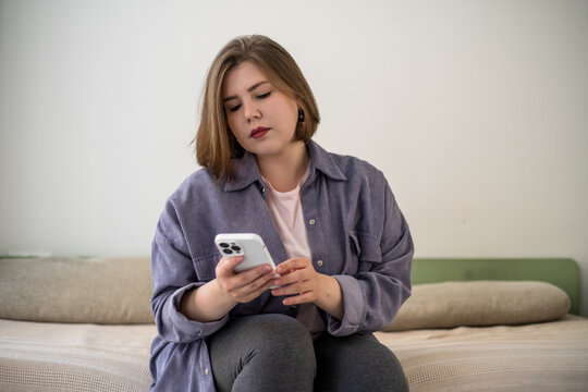 Plus size woman reading smartphone message on bed, screen time, online communication, personal news, waiting, digital stress, home lifestyle, remote contact.