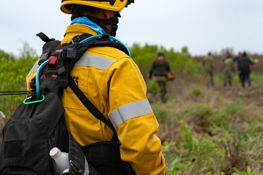 Wildland firefighter in yellow fire-resistant uniform with hydration pack looking at team during forest fire drill