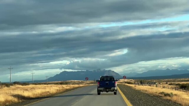 lue pickup truck driving on an empty road towards mountains in Chilean Patagonia