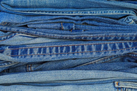 Denim fabric stacked in various shades of blue, showing the texture and patterns of the material in a close-up view