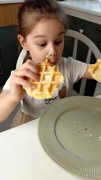 A beautiful young girl-child eats Belgian waffles with a happy face, smiles and laughs.