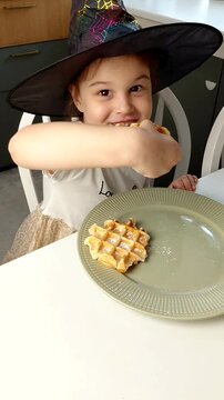 A beautiful young girl-child eats Belgian waffles with a happy face, smiles and laughs.