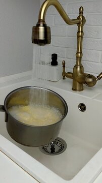 A woman rinses rice and millet in a pot under running water, close-up.