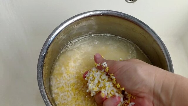 A woman rinses rice and millet in a pot under running water, close-up.