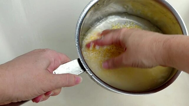 A woman rinses rice and millet in a pot under running water, close-up.