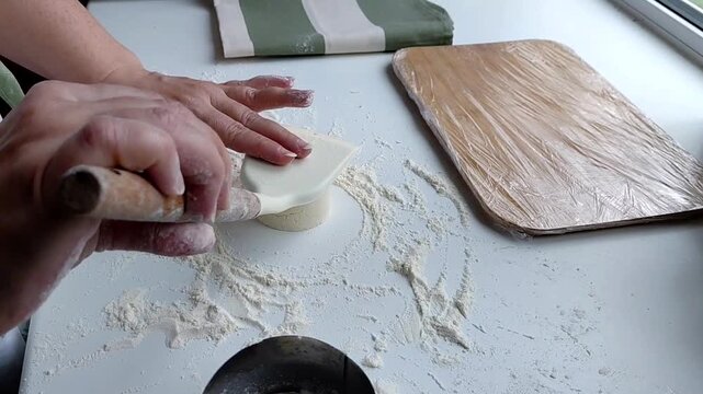 Hands of a female chef preparing homemade syrniki (cottage cheese pancakes) by coating them in flour on a wooden board before frying. Home cooking, traditional recipes, and culinary preparation.