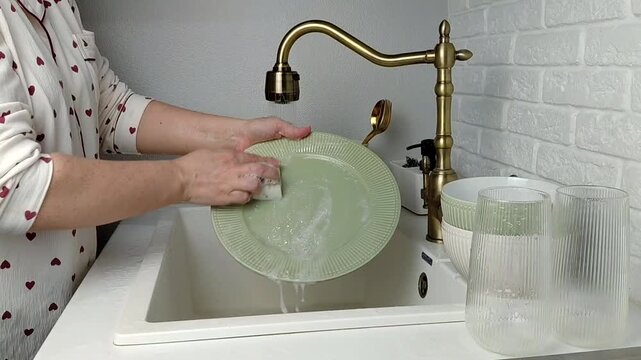 Woman washing dishes in kitchen sink, closeup. Cleaning chores