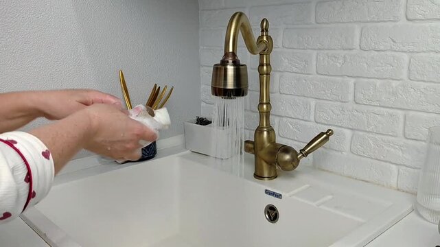 Woman washing dishes in kitchen sink, closeup. Cleaning chores