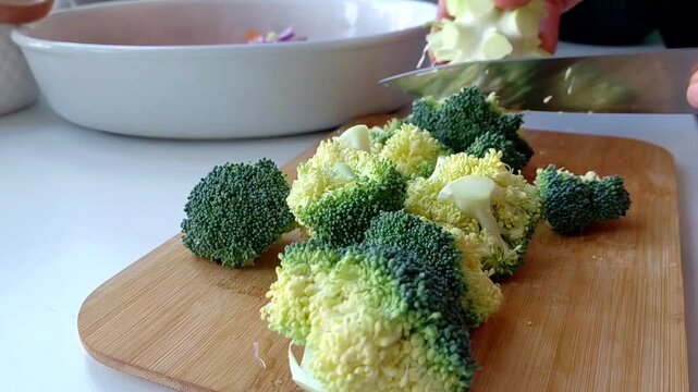 A man's hands are chopping fresh broccoli on the kitchen table. The close-up shot shows the preparation of healthy food with an emphasis on fresh vegetables and home cooking