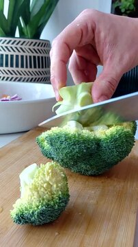 A man's hands are chopping fresh broccoli on the kitchen table. The close-up shot shows the preparation of healthy food with an emphasis on fresh vegetables and home cooking